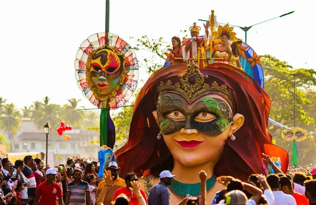 Carnival parade float with a giant masked figure, costumed performers, and a cheering crowd