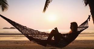 Person relaxing in a hammock on a beach at sunset with palm fronds overhead