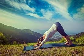 Woman doing downward-facing dog on a yoga mat on a hilltop with mountain views