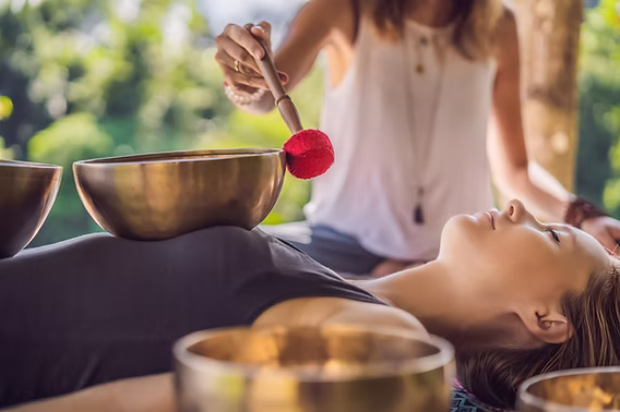 Woman lying down with a singing bowl on her stomach during a sound healing session