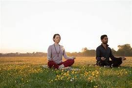 Man and woman meditating cross-legged in a meadow of yellow wildflowers at sunrise