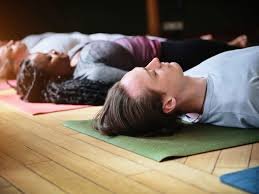 People lying on their backs on yoga mats in a relaxation pose on a wooden floor