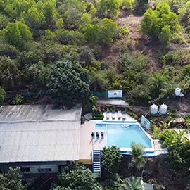 Aerial view of a retreat building and swimming pool on a forested hillside