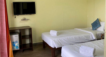 Twin guest room with two single beds, folded towels, and a wall-mounted TV