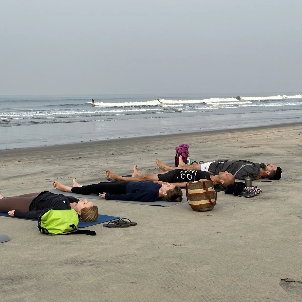Students resting in savasana on the beach after yoga practice in Goa